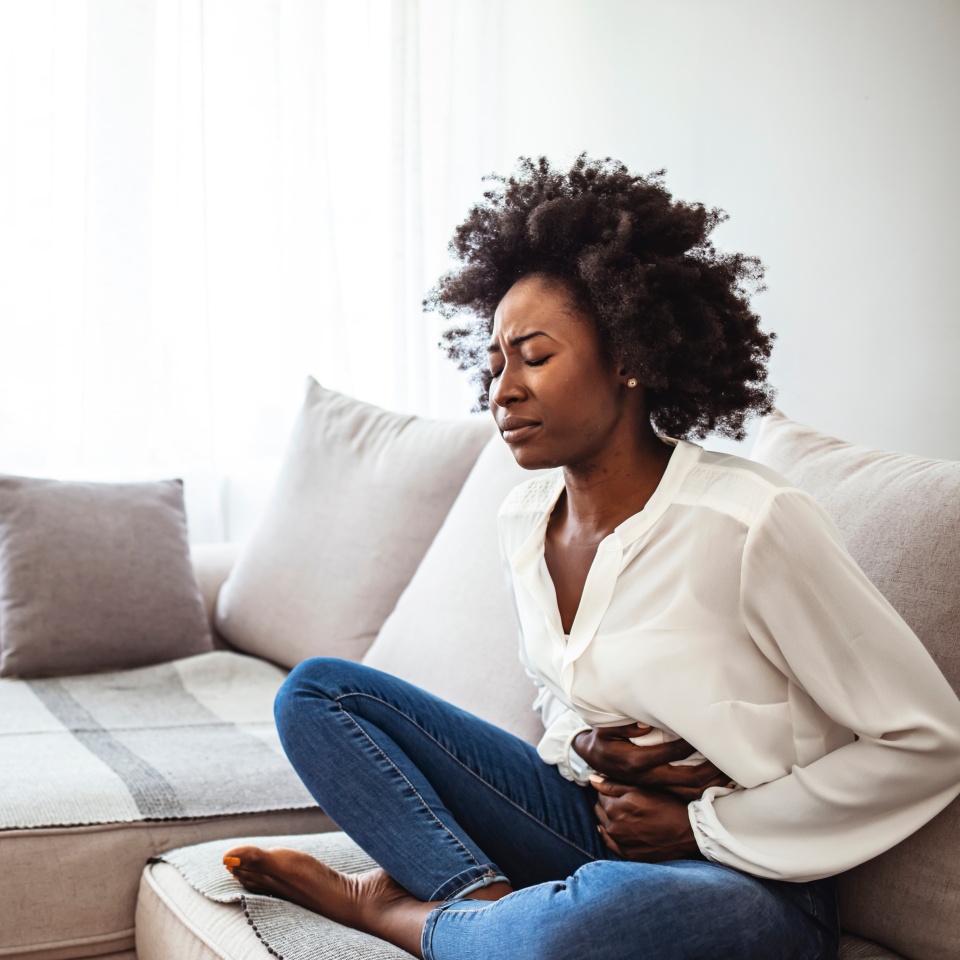 Shot of an attractive young woman suffering from stomach cramps at home. Young woman suffering from strong abdominal pain while sitting on sofa at home