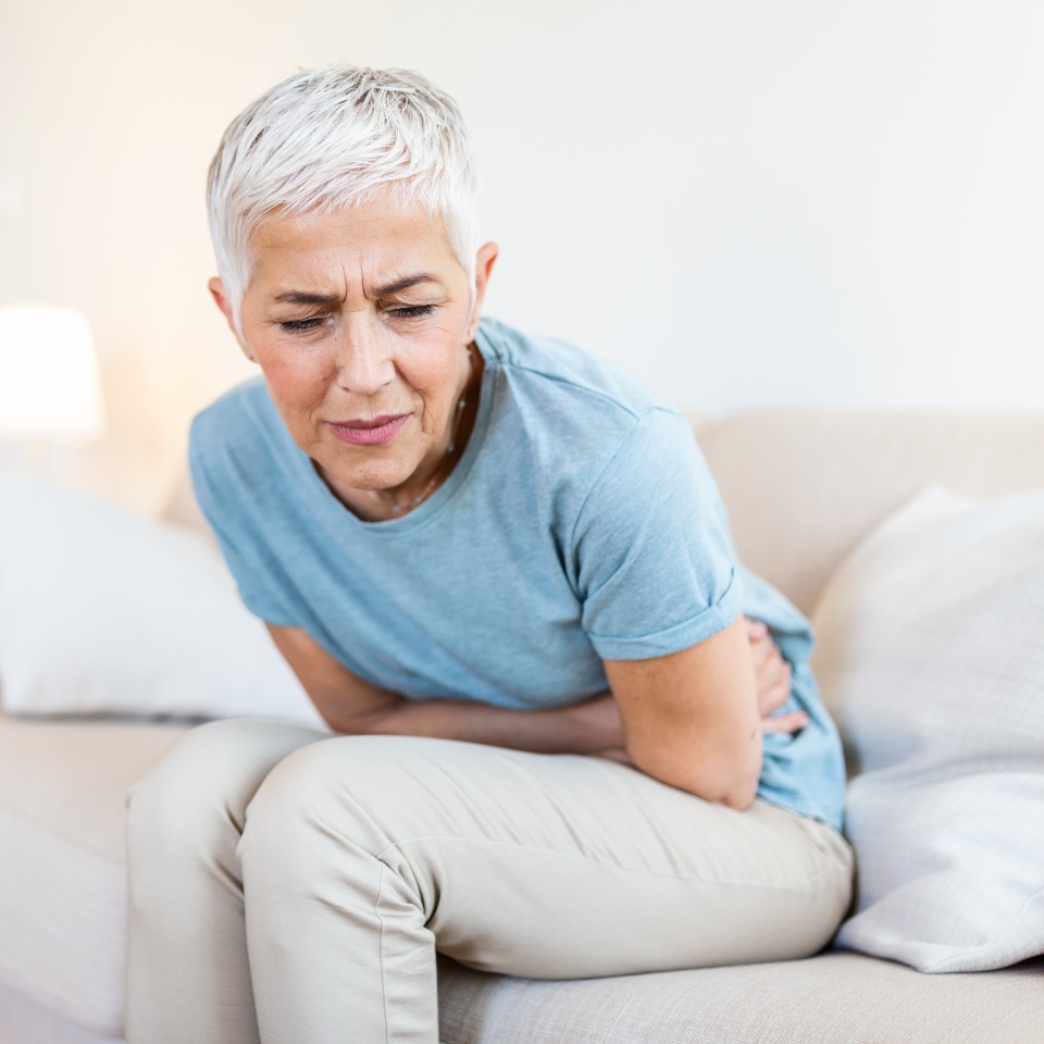 Middle-aged woman sitting on bed feels unhealthy touch stomach suffers from severe crampy abdominal pain,