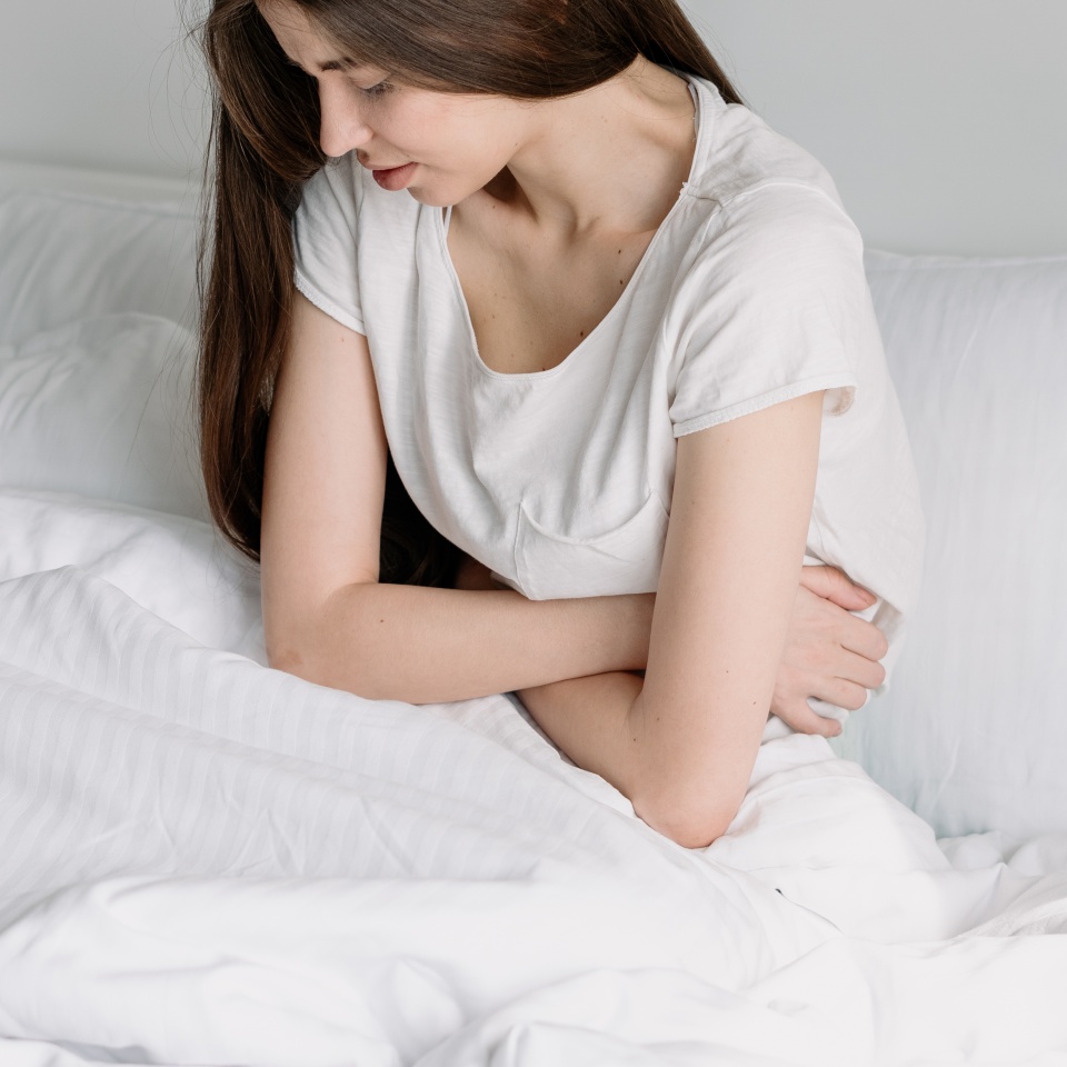 Health problem concept. Side view of sick young woman in pajamas sitting on bed, touch belly, suffer from stomach ache. Ill millennial girl struggle with periods pain spending morning in bedroom