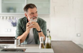 Happy mature man drinking coffee at home in the kitchen, enjoying hot drink in the morning on weekend