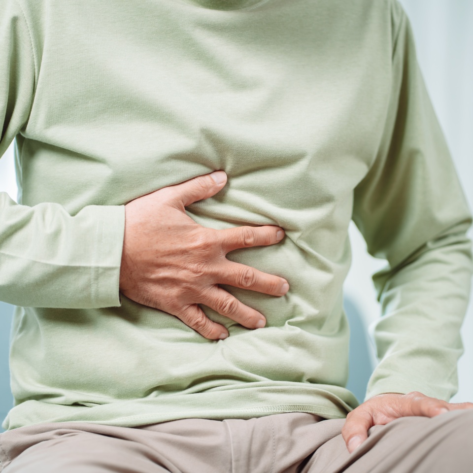 Asian Senior man feel stomachache. Older mature male touch belly while sitting on sofa in living room at home. Bowel problem health care and medical insurance concept.