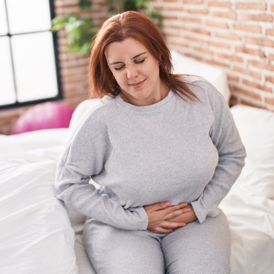 Young beautiful plus size woman suffering for menstrual pain sitting on bed at bedroom