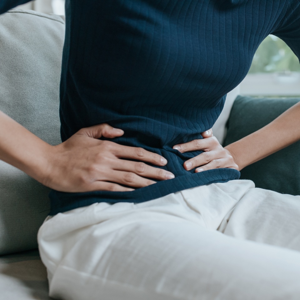 Portrait close-up of young woman suffering from pain in the stomach while sitting on the sofa in the living room. Health care and medical concepts.