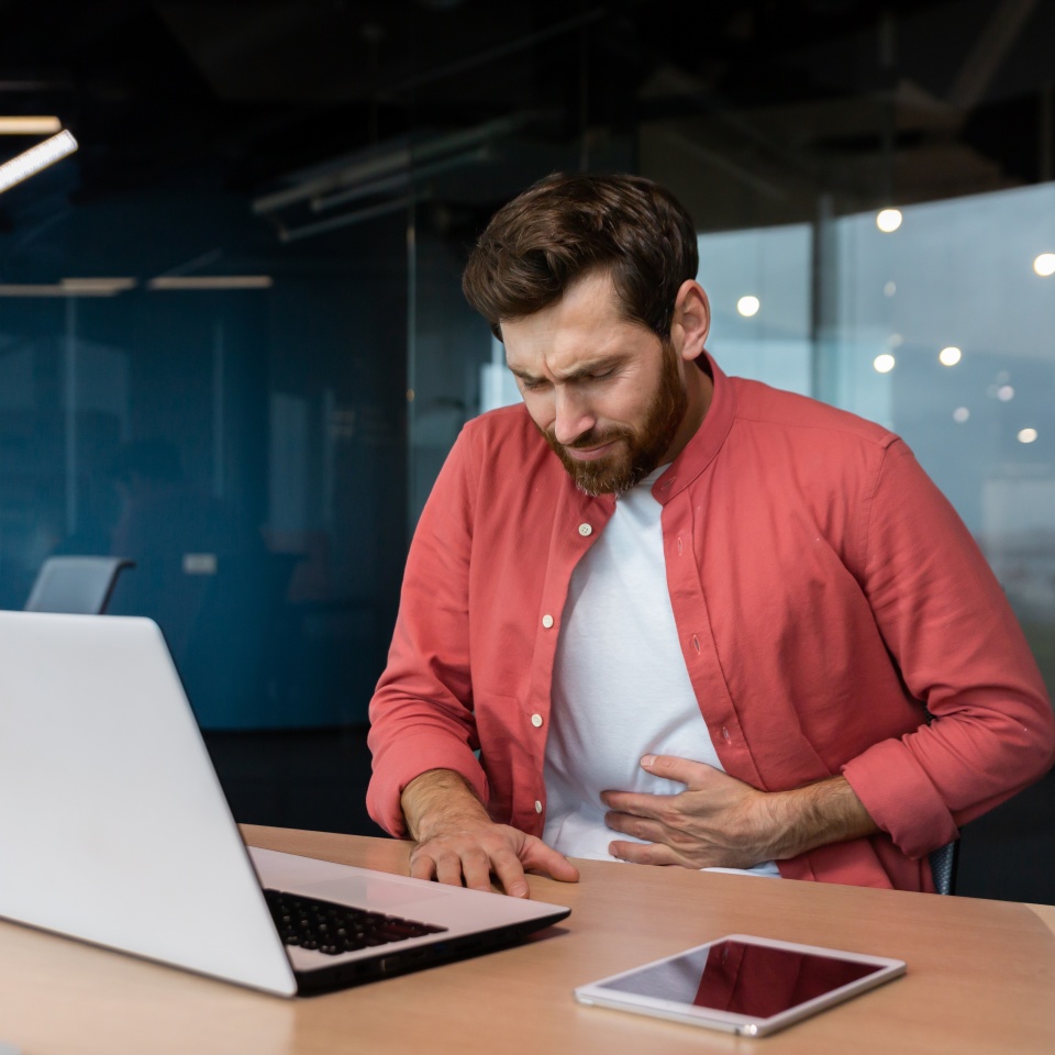 A man in the office at the workplace is sick, he has a severe stomach ache, the businessman got food poisoning from lunch, he is sitting at the table inside the building.