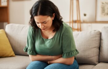 Stress, stomach pain and woman on a sofa with menstruation, gas or constipation, pms or nausea at home. Gut health, anxiety and lady with tummy ache in living room from ibs, bloated or endometriosis