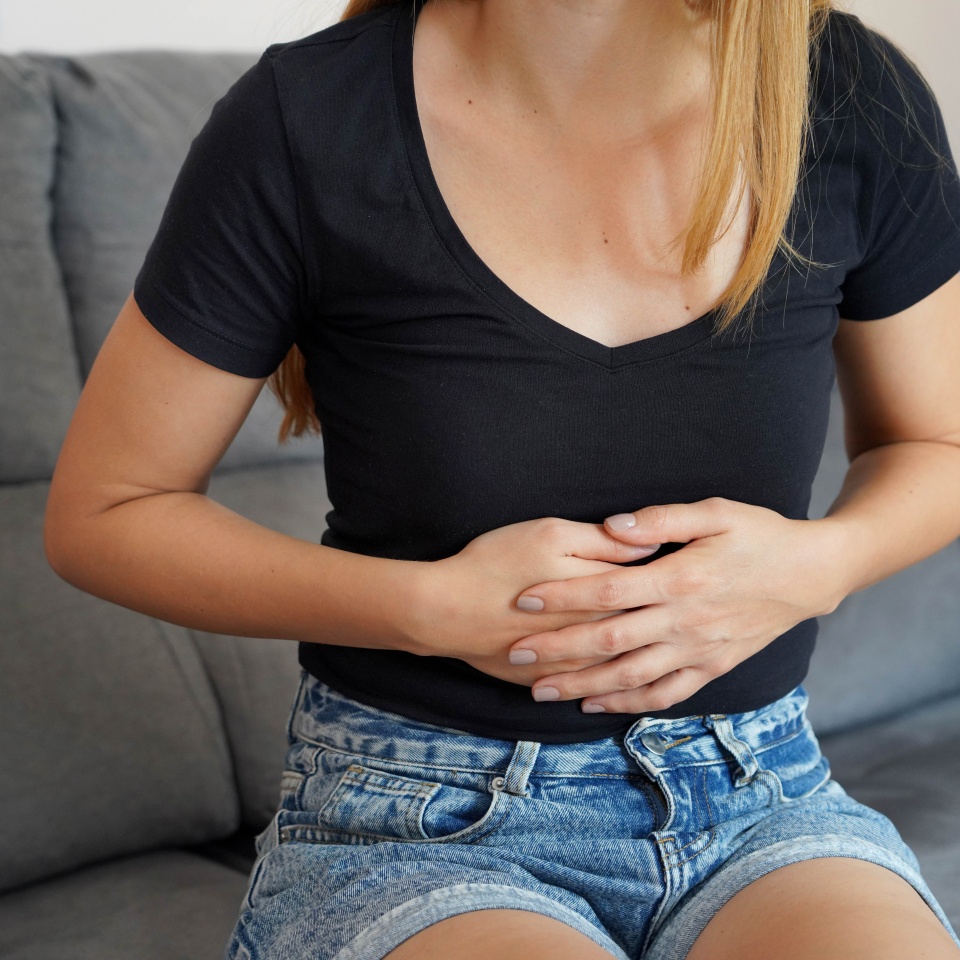 Digestive problems from poor diet. Young woman suffering from strong abdominal pain while sitting on sofa at home.