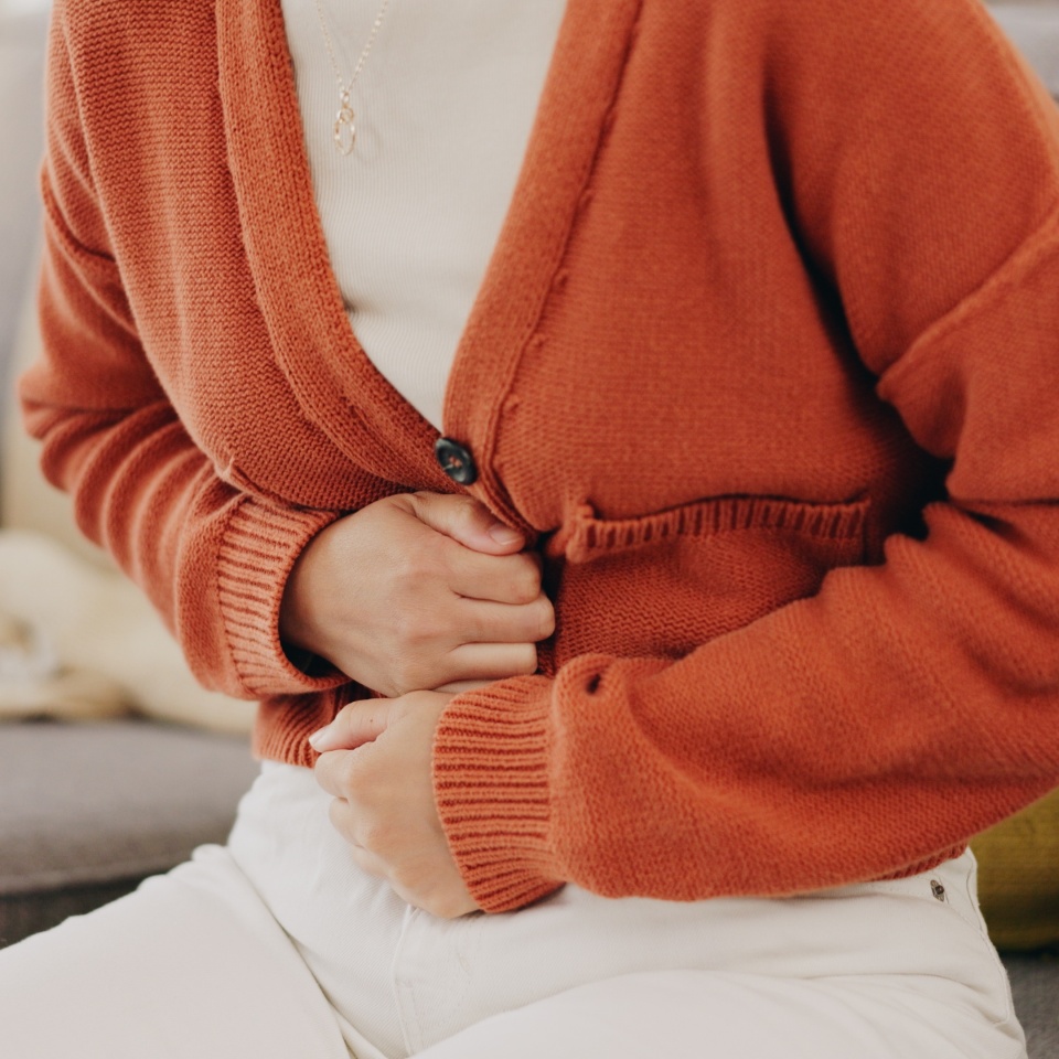 Stomach ache, cramps and hands of woman with abdomen pain due to constipation, menstruation or ibs issue. Sick, home and person suffering and holding belly in a house lounge, couch and living room