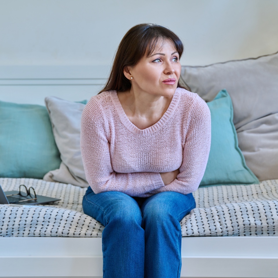 Middle aged woman experiencing abdominal pain sitting on couch at home