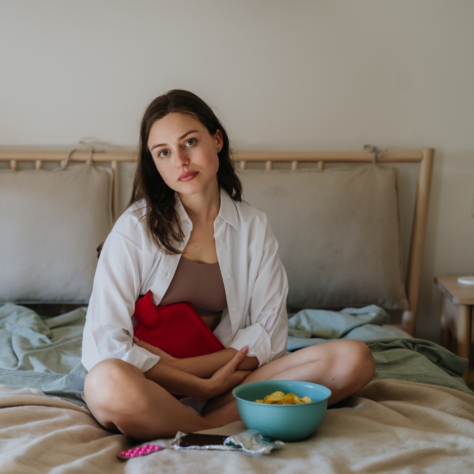 Woman at home suffering from menstrual pain, having cramps. Woman warming lower abdomen with a hot water bottle, endometriosis, and conditions causing pain in tummy.