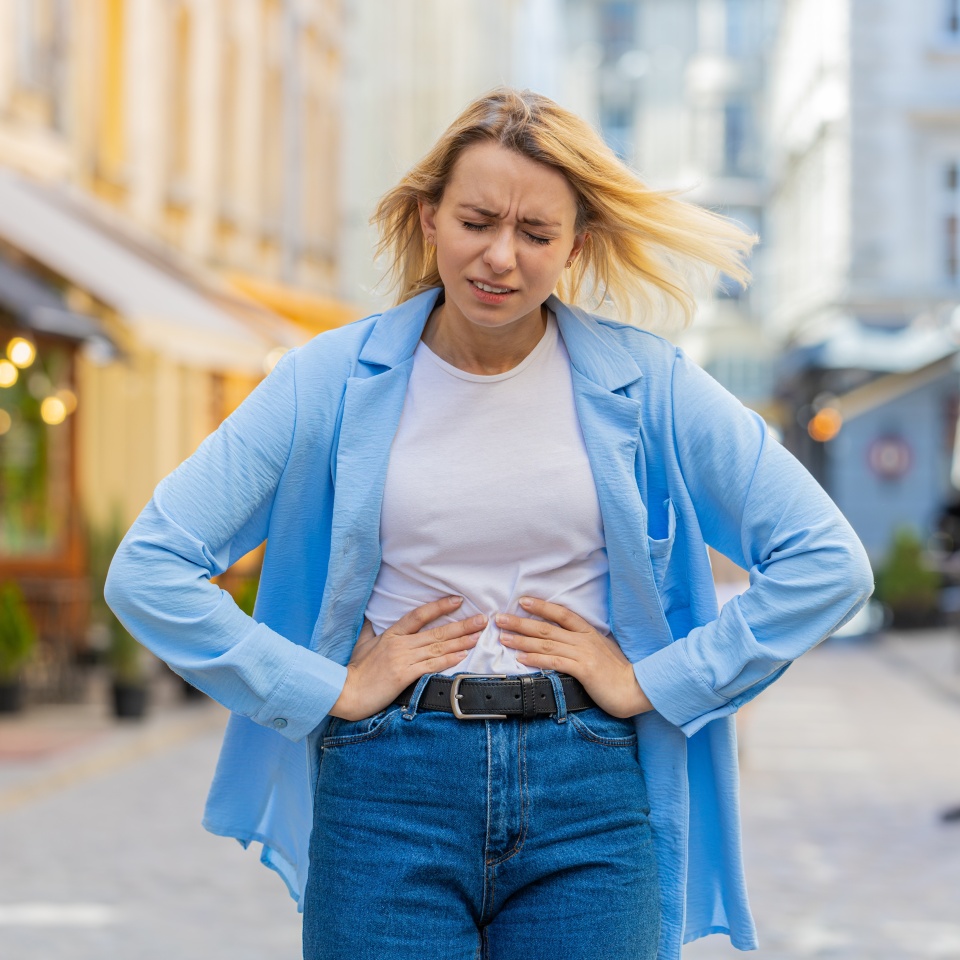 Caucasian young woman traveler feeling sudden strong abdominal stomach ache gastritis problem. Upset tourist lady having symptom poisoning diarrhea indigestion peptic ulcer pancreatitis on city street