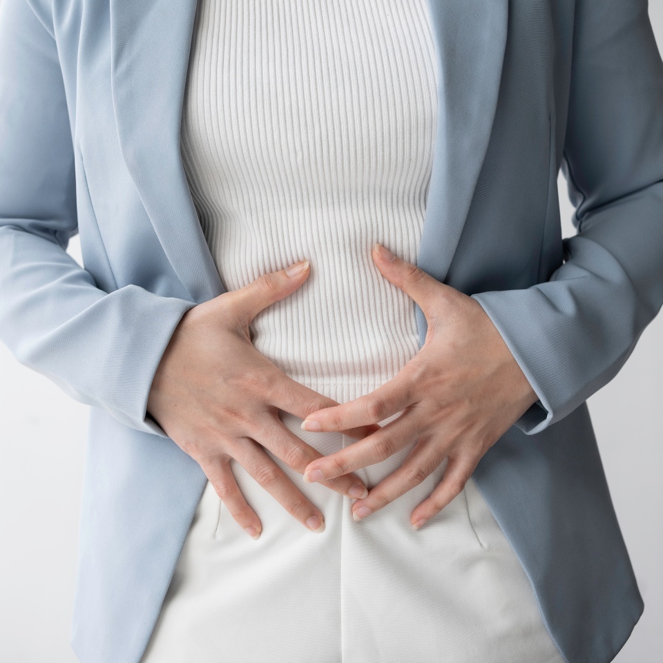 Businesswoman is standing in her office, holding her stomach in pain, possibly experiencing menstrual cramps or digestive problems