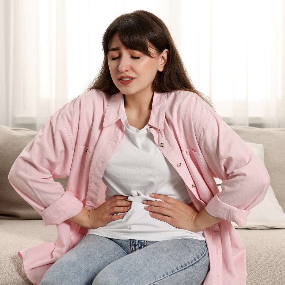 Upset woman suffering from abdominal pain on sofa at home