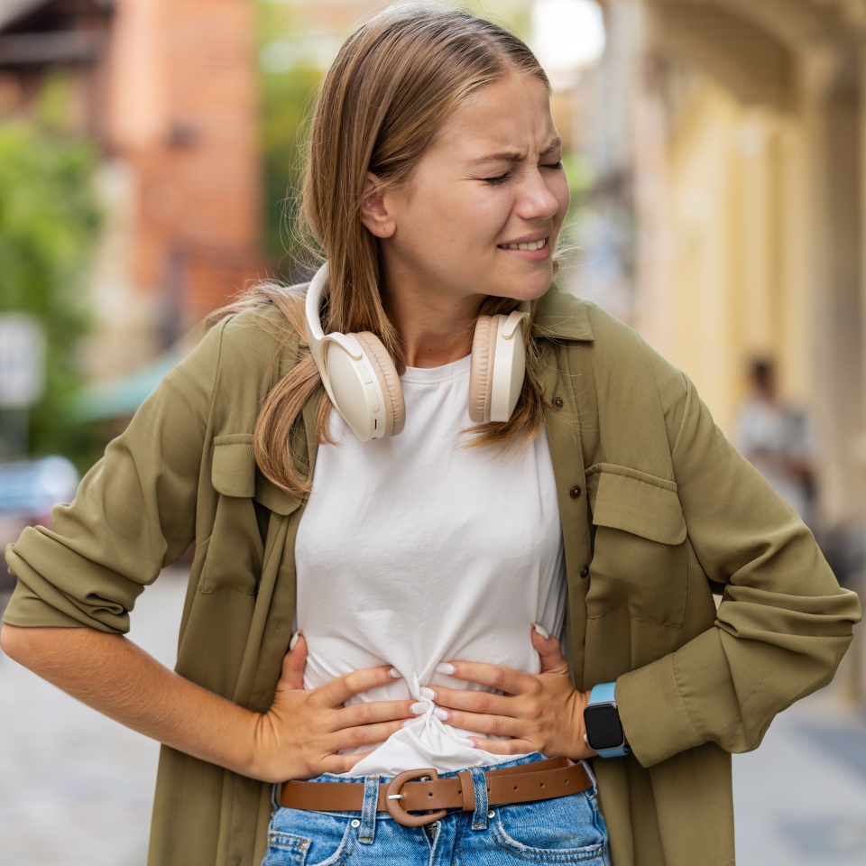Caucasian young woman traveler feeling sudden strong abdominal stomach ache, gastritis problem. Upset tourist having symptom poisoning diarrhea indigestion peptic ulcer pancreatitis on city street.