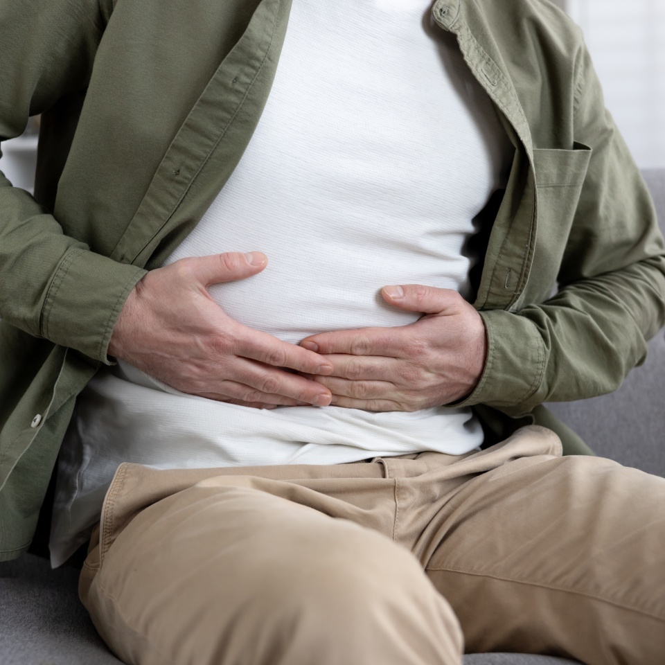 Man sitting on couch experiencing abdominal pain holding stomach. Wearing casual clothing and showing visible discomfort. Concept of stomachache, digestive issues, or health concerns.