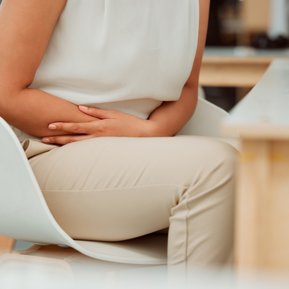Business woman, hands and stomach ache with pain, digestion or sore gut on chair at office. Closeup, female person or employee with gastro, reflux or abdominal cramps for period or menstrual cycle