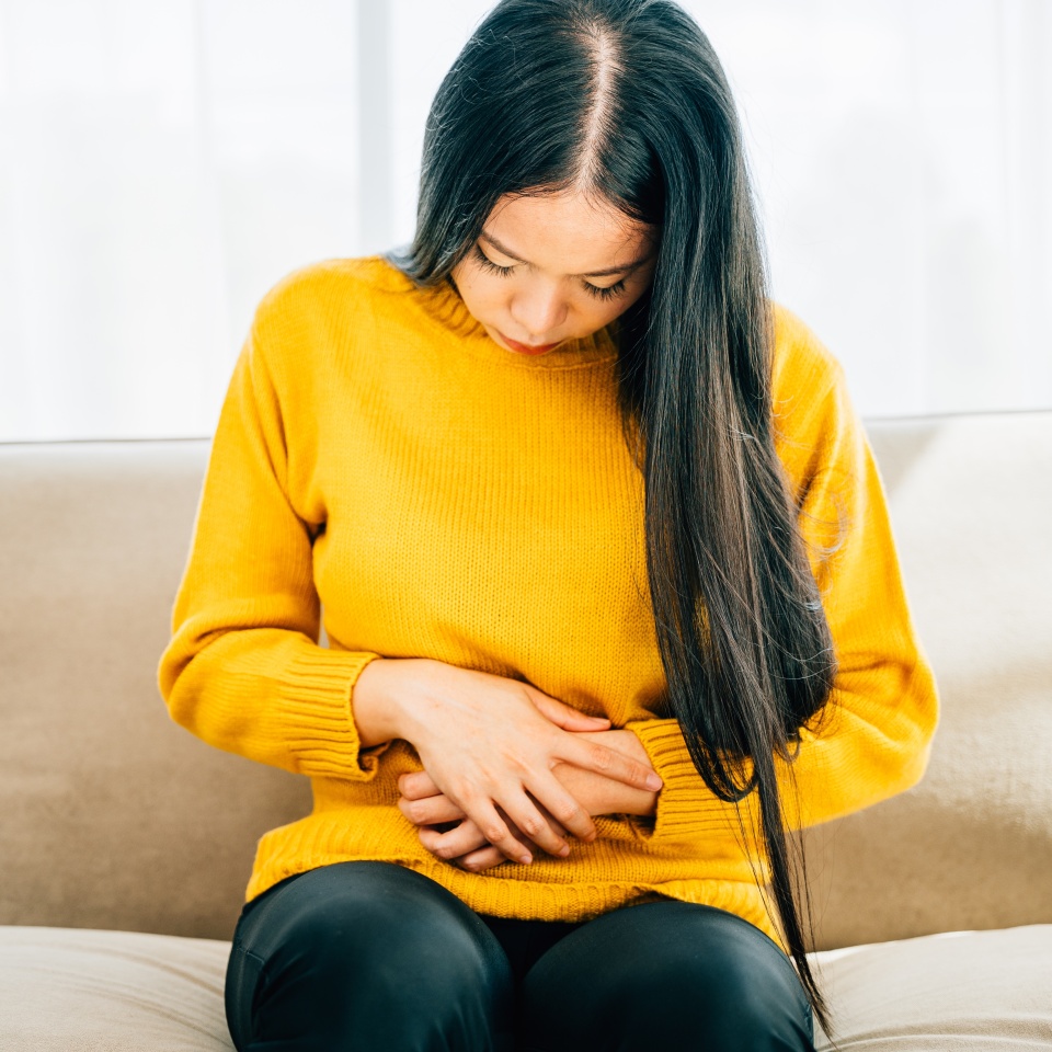 Illustrating stomachache, Young woman sitting on a sofa suffering from severe abdominal pain. Emphasizing discomfort symptoms and care for abdominal health. Health care abdomen bloating concept