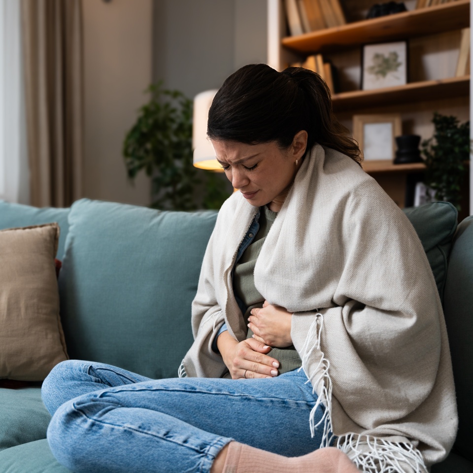 Stomach ache, cramps and hands of woman with abdomen pain due to constipation, menstruation or ibs issue. Sick, home and person suffering and holding belly in a house lounge, couch and living room