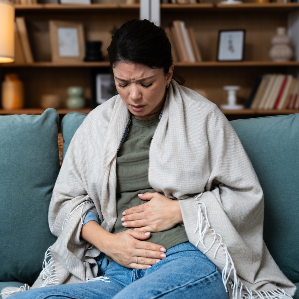 Stomach ache, cramps and hands of woman with abdomen pain due to constipation, menstruation or ibs issue. Sick, home and person suffering and holding belly in a house lounge, couch and living room