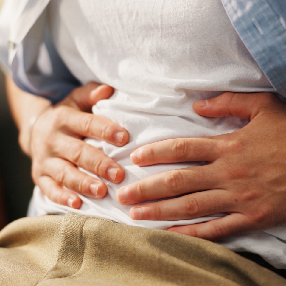 Stomachache, hands and person in home, pain and man with food poisoning in living room or indigestion. Abdominal, cramps and discomfort on couch, gas and bloating in lounge, diarrhea or constipation