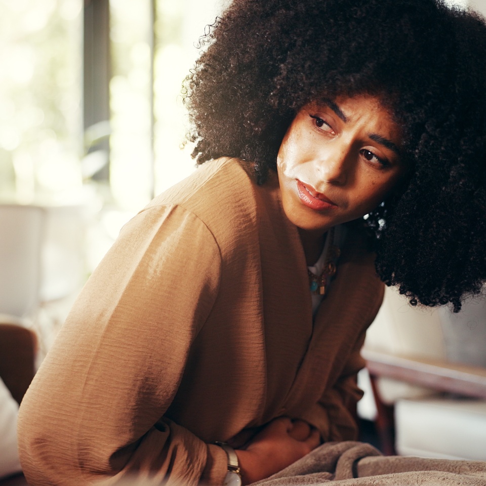 Girl, stomach and cramps or pain on sofa for menstruation, ovarian cysts and discomfort in lounge. Woman, home and abdominal ache for monthly cycle, period and tension or strain in house living room