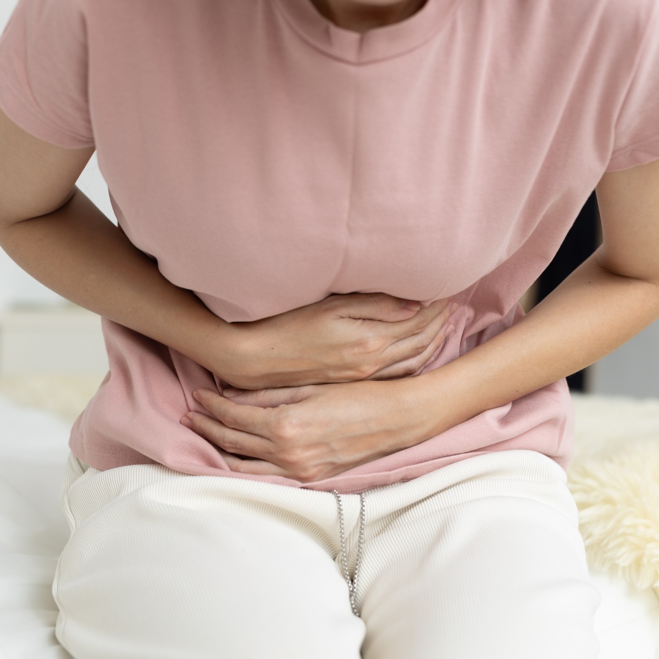 women bending over in pain from stomach cramps while sitting on bed. Concept of digestive issues, menstrual cramps, or abdominal discomfort at home in daily life.