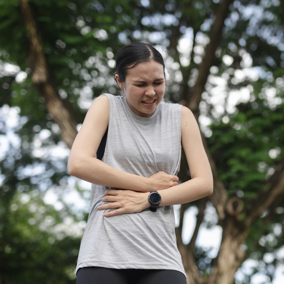 women experiencing severe abdominal pain outdoors, possibly due to stomach cramps, indigestion, food poisoning or health emergency. Concept for digestive problems, discomfort.