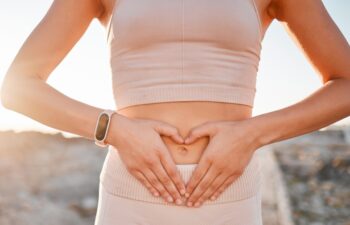 Woman, heart and hands on stomach for fitness, weightloss diet or holistic gut wellness. Closeup female abdomen, love fingers or belly emoji of body digestion, skincare and healthy exercise in nature