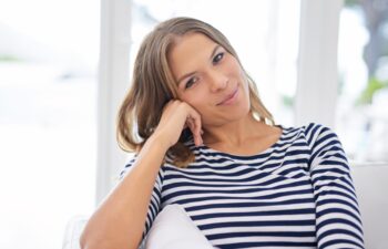 Portrait, house and woman on sofa, comfort and happiness with weekend break, relax and peaceful. Face, apartment and cheerful person on couch, girl and joyful with wellness, calm or resting in lounge